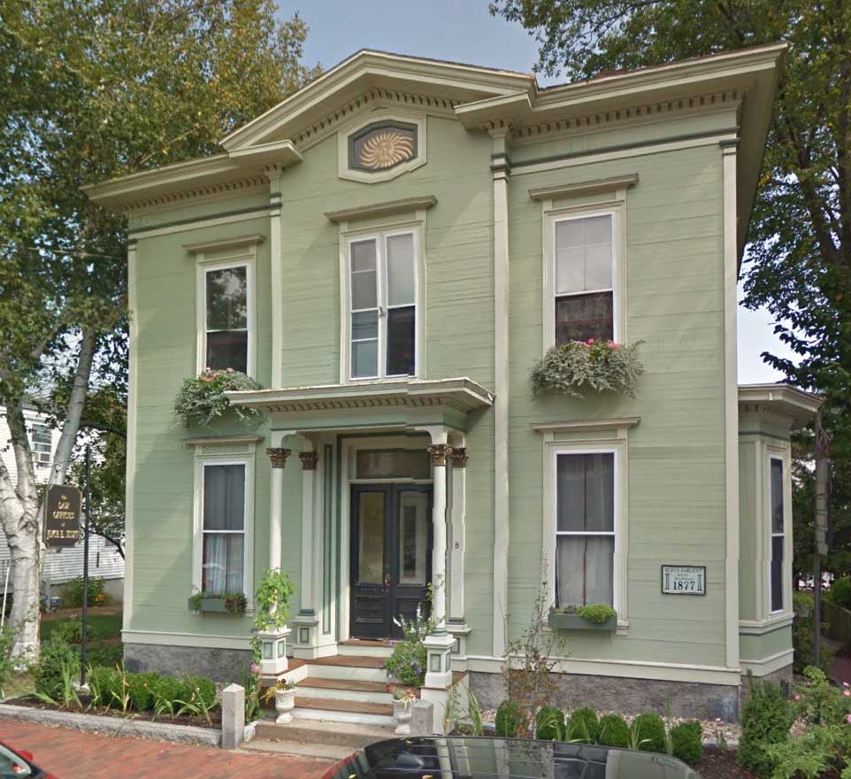 A large green house with a porch and a brick walkway.